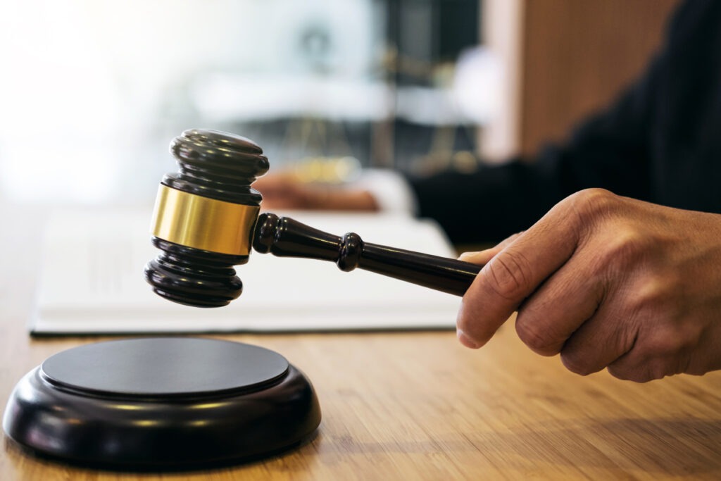 A judge's hand raises a gavel above a wooden block, signifying a legal decision in a courtroom setting.